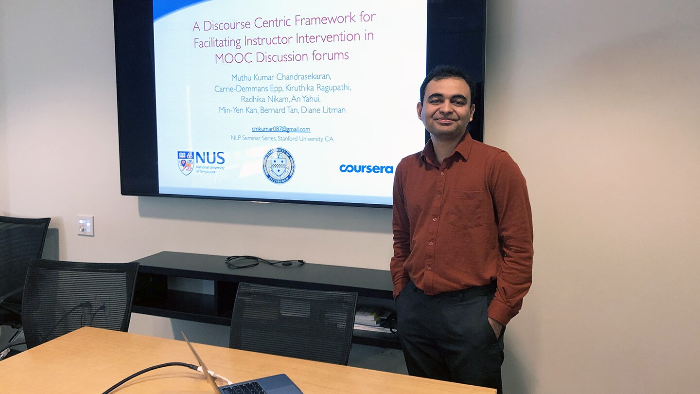 Muthu Kumar Chandrasekaran, applied science manager at Amazon, stands near a large display screen with a slide showing the title of a presentation