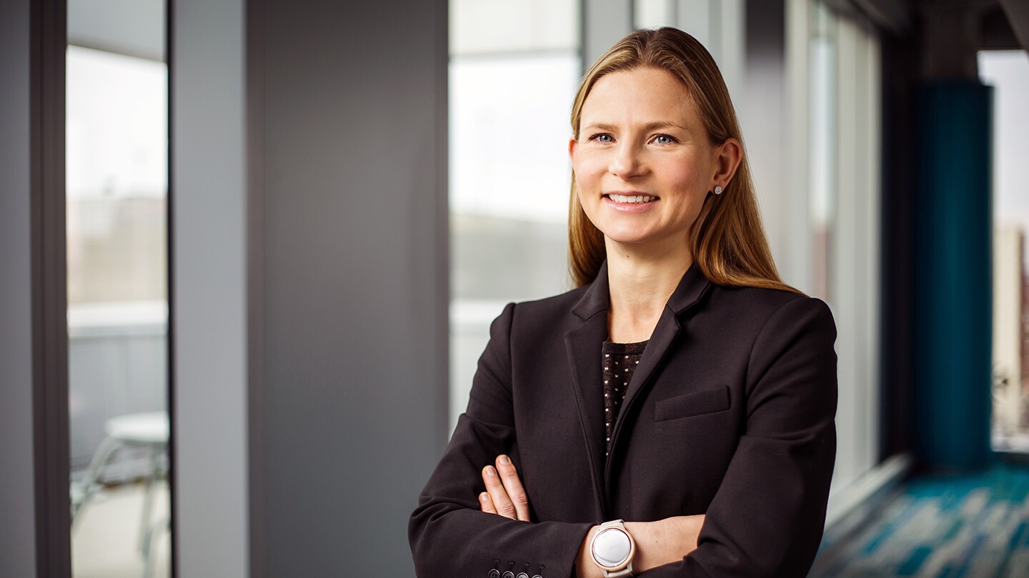 Jessie Handbury, an associate professor at University of Pennsylvania and Amazon Visiting Academic, is seen smiling with her arms crossed in a profile photo, there are large windows in the background