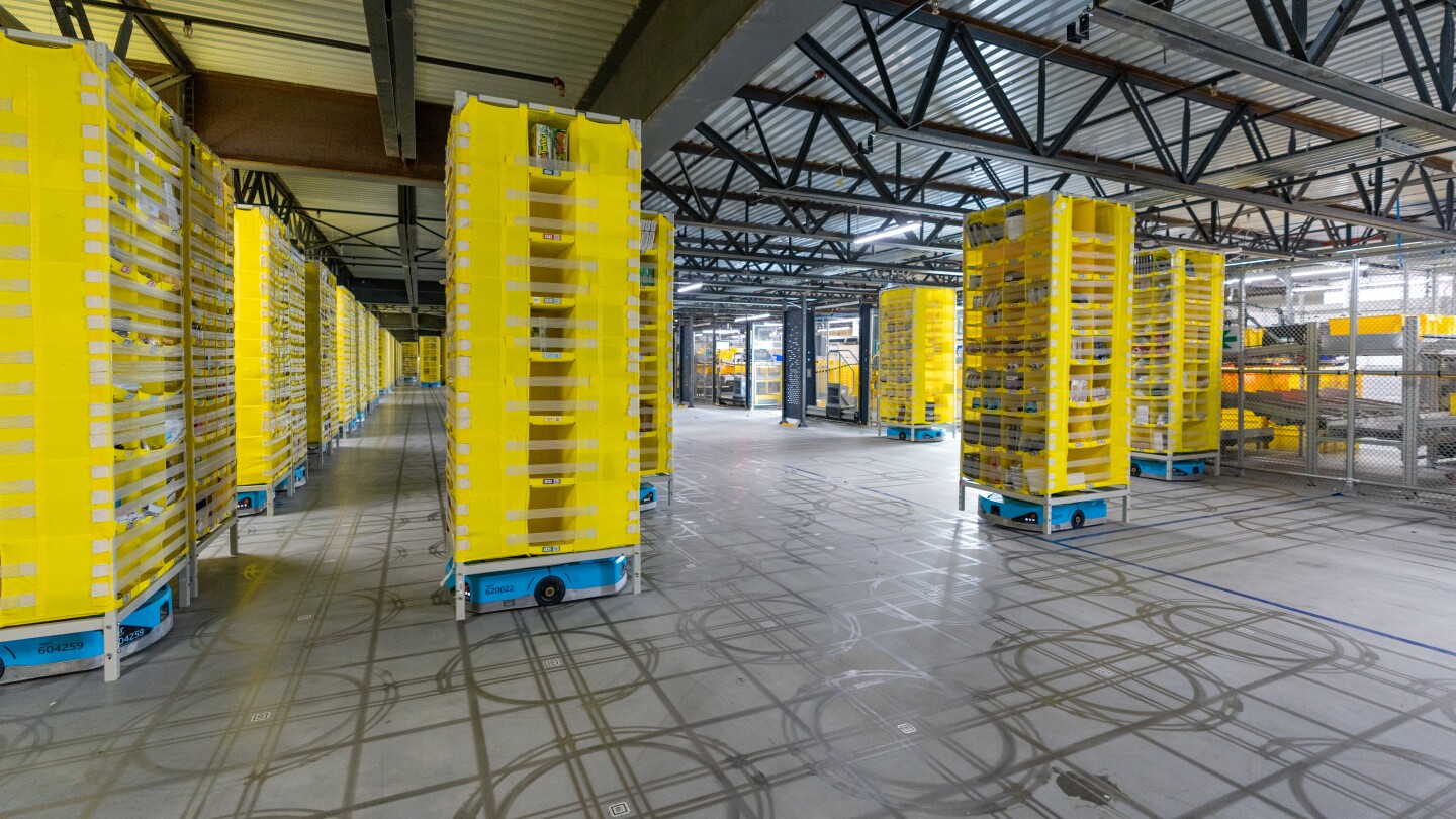 Several small blue Hercules robots are seen transporting tall yellow pods in a fulfillment center