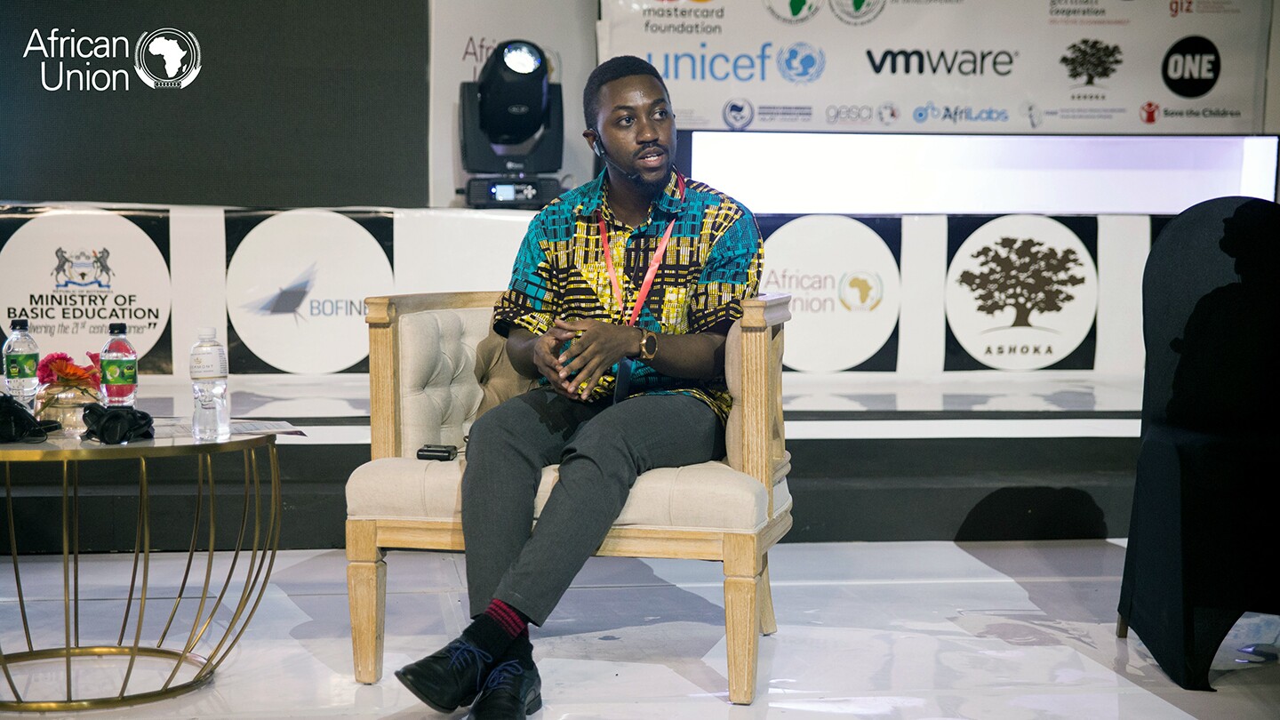 George Boateng is seen sitting on a chair on a stage while speaking on a panel about his SuaCode work at the African Union’s  2019 Innovating Education in Africa Expo in Gaborone, Botswana.