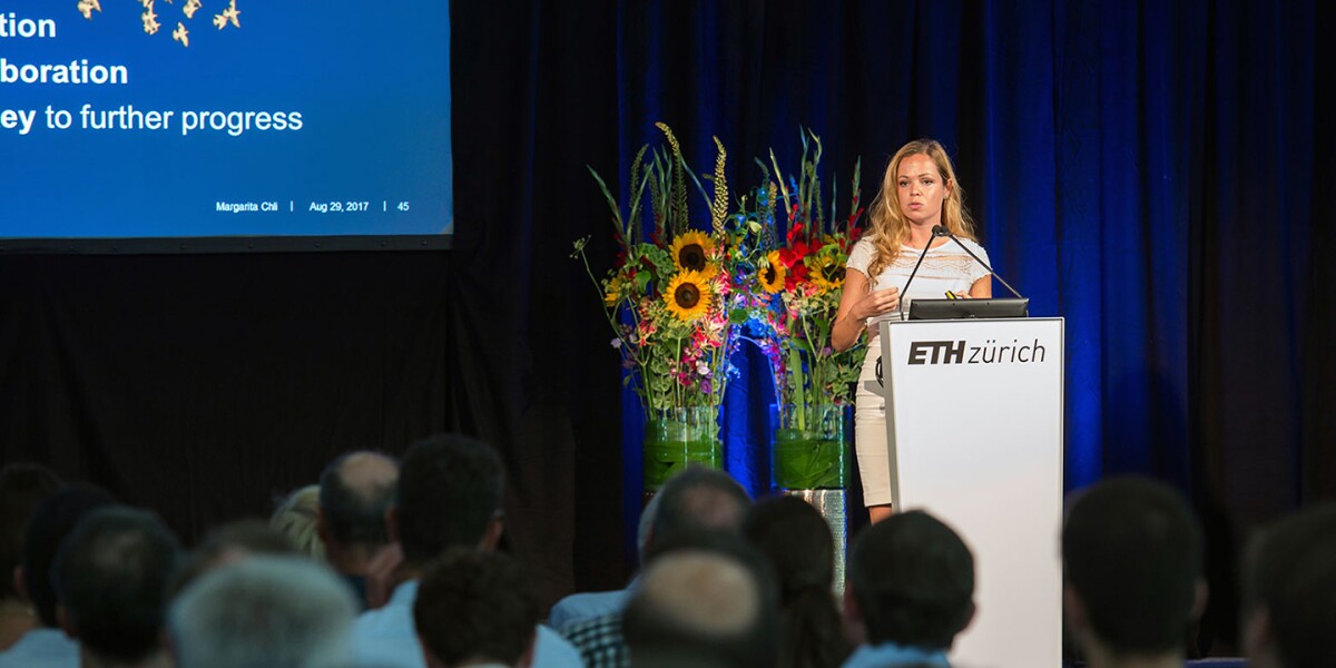 Margarita Chli is seen speaking behind a lectern that says ETH Zürich on it, there are two large flower vases just behind her