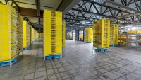 Several small blue Hercules robots are seen transporting tall yellow pods in a fulfillment center