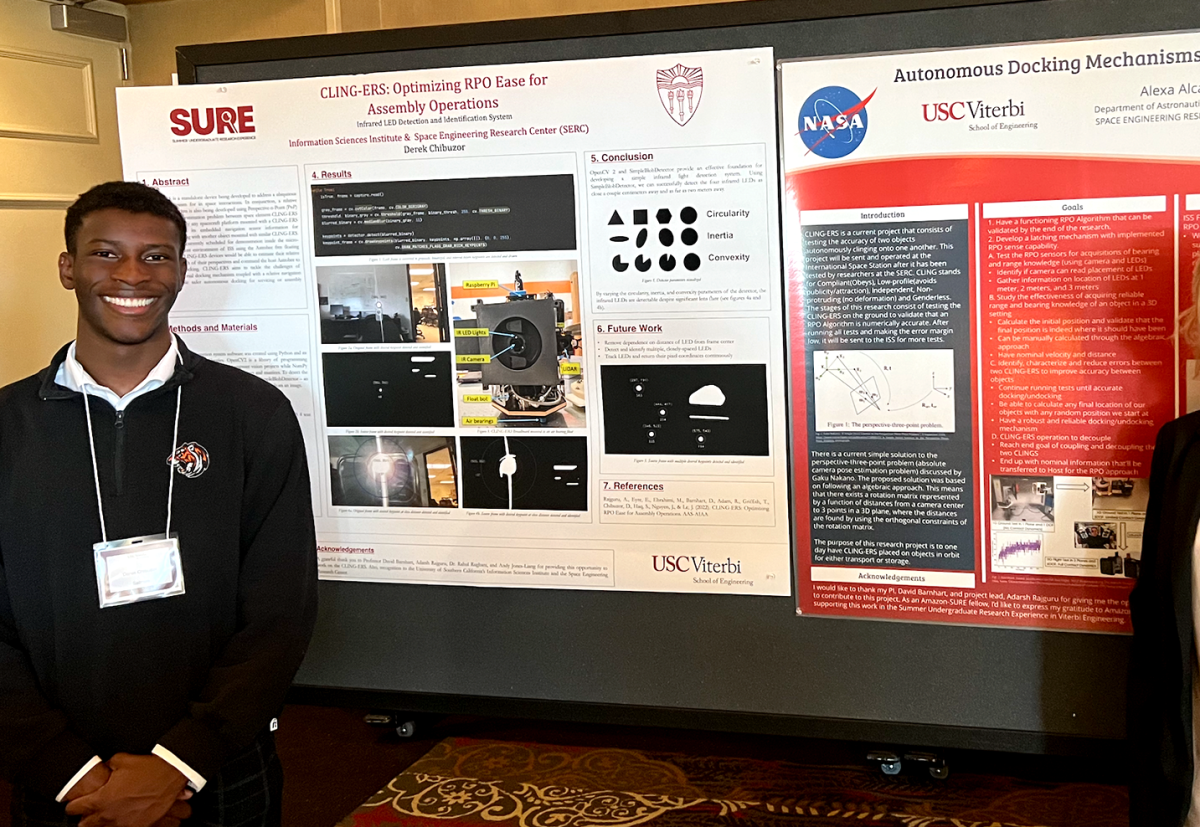 Derek Chibuzor. left, is seen standing in front of some posters that were part of a presentation for a project called “CLING-ERS” which had the goal of developing an autonomous spacecraft docking solution for the International Space Station.