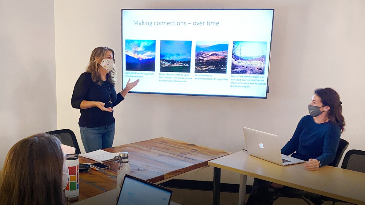 Lise St. Denis is seen wearing a mask and standing, on the left, while teaching a recent graduate seminar. There is a display screen behind her and two students, also masked, are seen sitting.