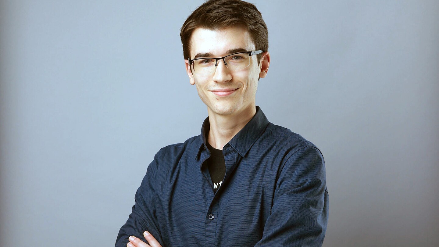 Edouard Belval is seen smiling and crossing his arms while posing for a portrait photo 