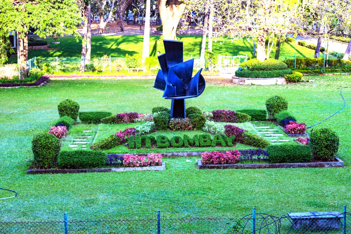 A sculpture is seen in the middle of a garden, including a row of plants sculpted to spell out IIT Bombay