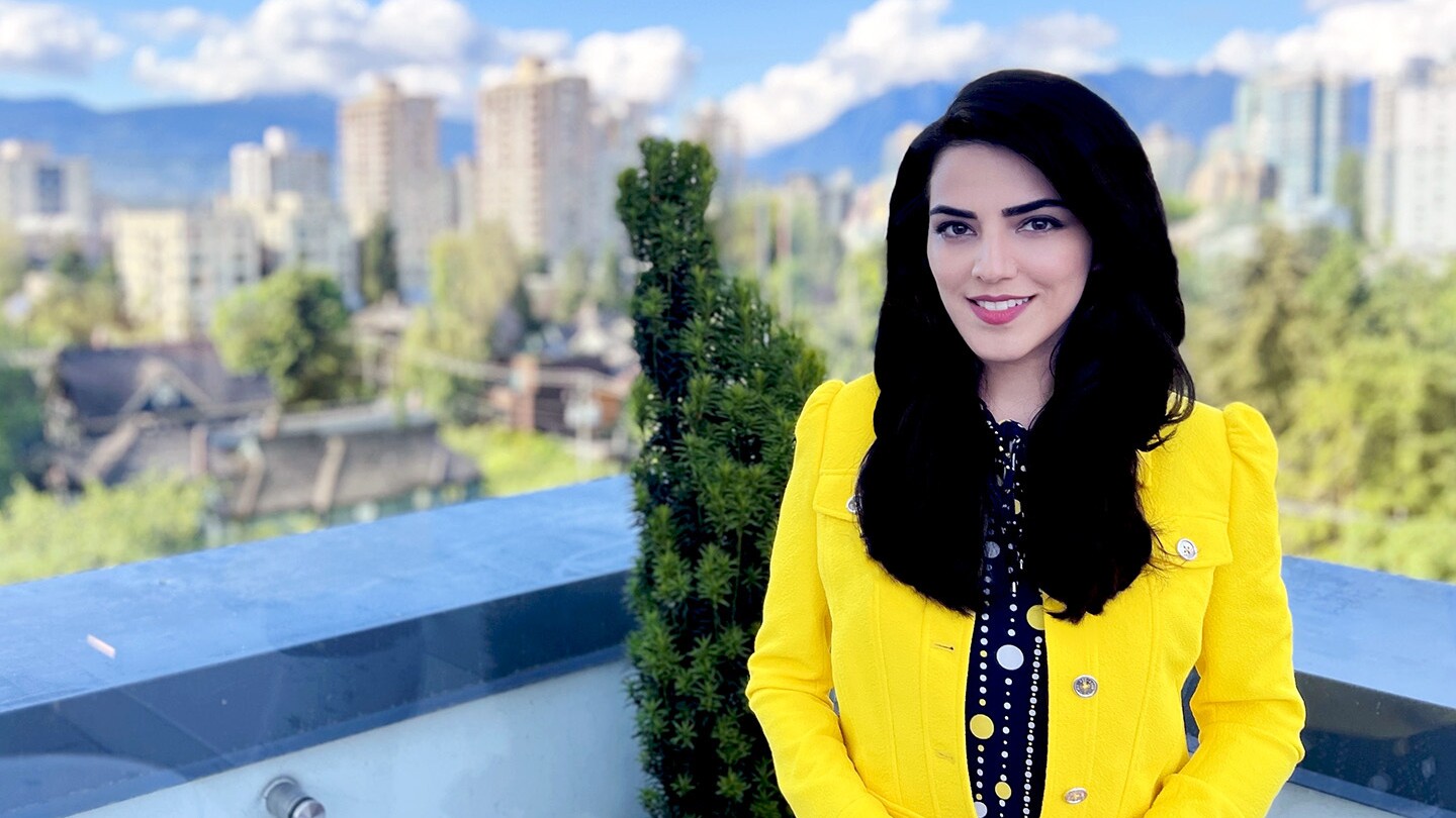 Parmida Beigi, an Amazon senior research scientist, is seen smiling into the camera on a sunny day, she is standing on a terrace with houses and a cityscape visible in the background