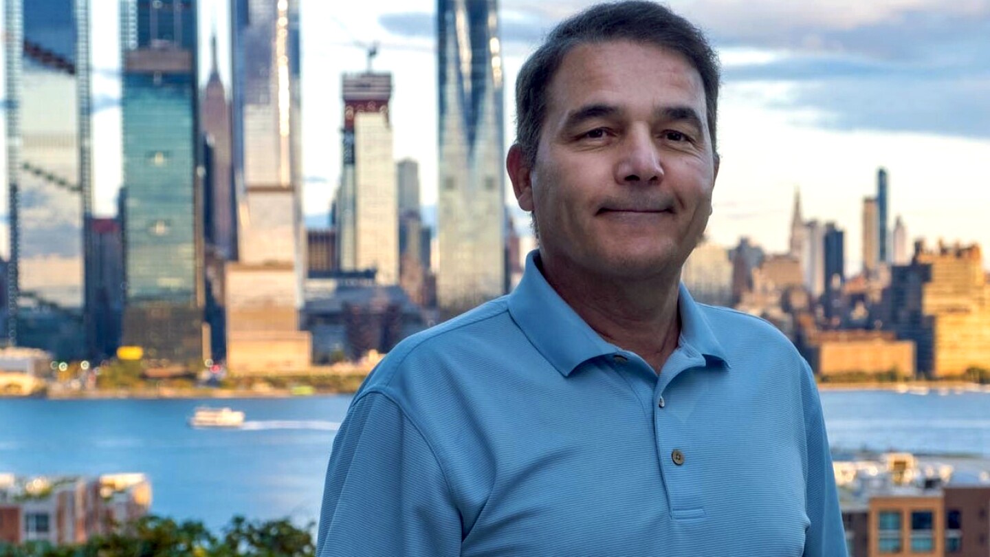 Anwar Walid, an Amazon applied science manager, is seen looking into a camera, there is a river and city skyline in the background