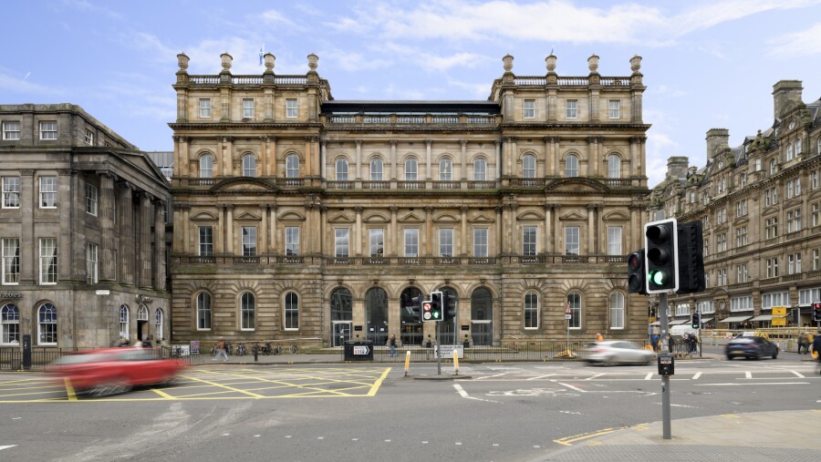 A view of the entrance into the office building in Edinburgh, Scotland, featuring moving cars and a green traffic light 