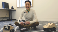 Amanda Prorok is seen sitting on a floor in her lab at the University of Cambridge, she is surrounded by some mobile robots