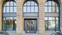 A zoomed-in view of the double-door entrance into the Berlin office building, there are large glass windows above the door and to either side and some bikes parked out front