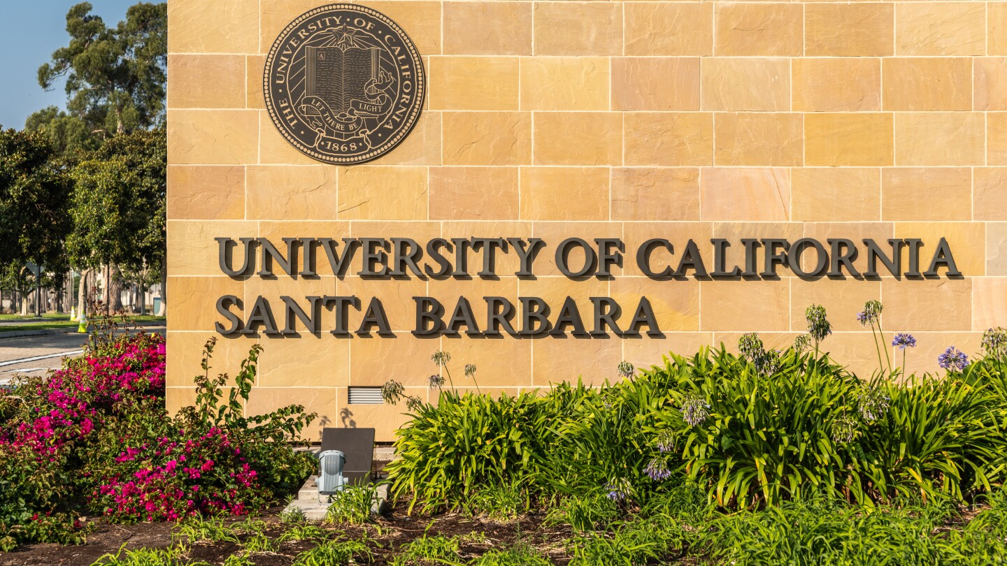 A portion of an entrance to the University of California Santa Barbara is seen, with the university name and seal on a brick wall 