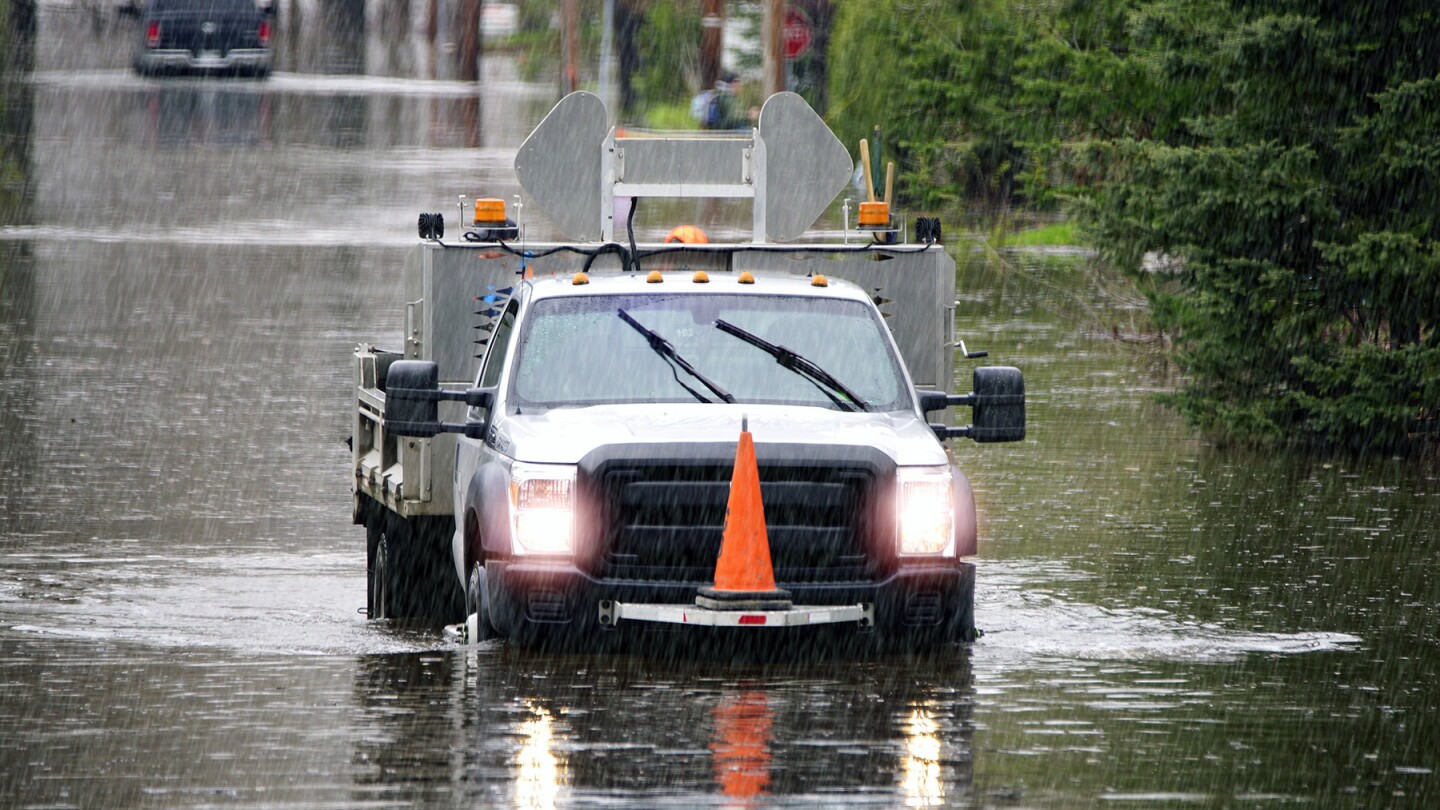 A city crew truck is seen driving down a flooded street in a downpour