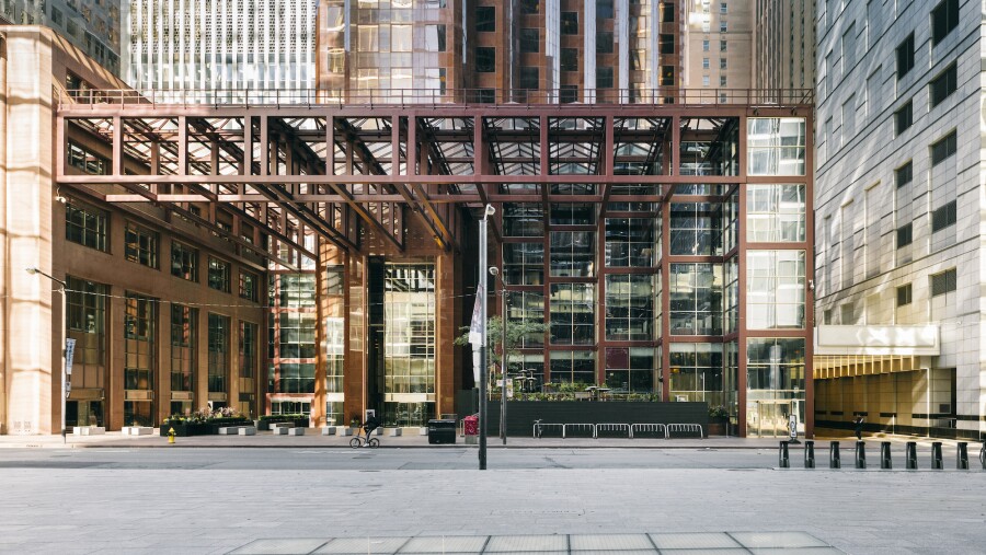 A street view of the entrance into the building in Toronto, Ontario, including bike racks, stone seating, and the building's unique metal scaffolding 