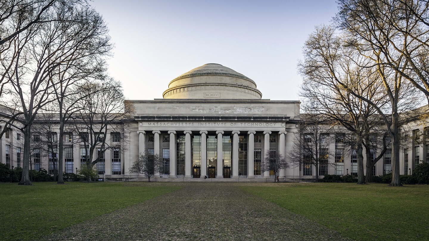 View of the Massachusetts Institute of Technology in Cambridge, showcasing the architecture of its main building with an expansive green lawn in the foreground on a sunny autumn day.