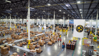 An aerial view of the inside an Amazon facility, there are rows of boxes and tables with workers moving among them