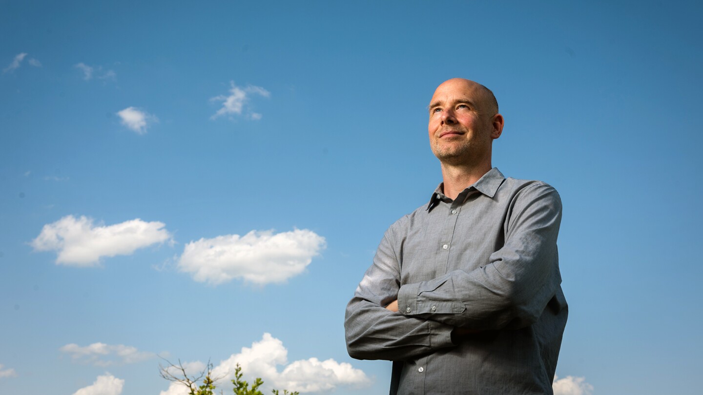 Philip Stier, the head of Atmospheric, Oceanic and Planetary Physics at the University of Oxford, is seen standing with his arms folded under a blue sky with some clouds in the background.