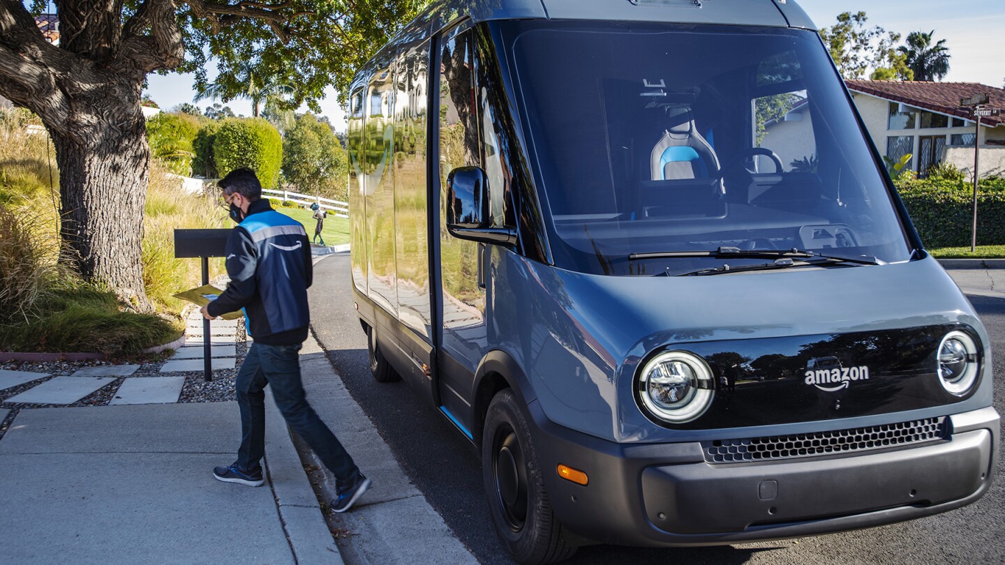 An Amazon employee is seen making a delivery while an electric delivery van is parked behind him on a residential street in Los Angeles