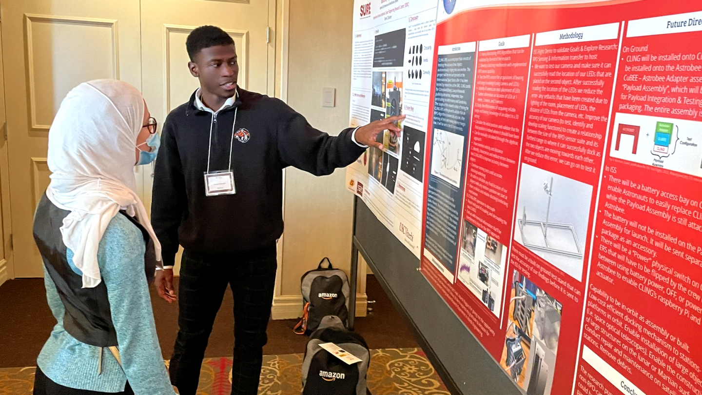 Derek Chibuzor, who is pursuing a masters in electrical engineering with an emphasis in machine learning and data science at USC, is seen pointing to a poster while another person listens to his explanation.