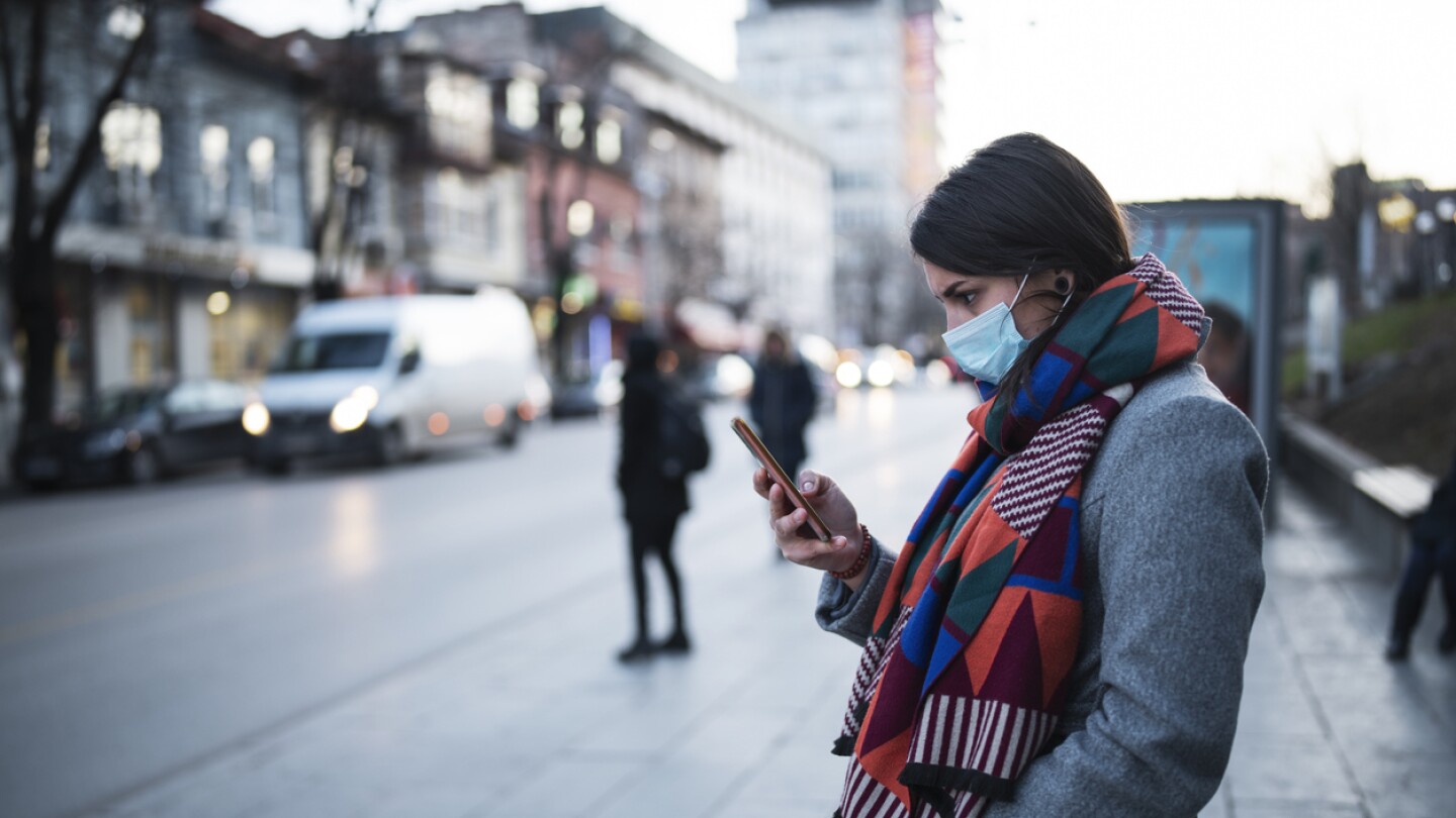 woman standing on sidewalk wearing face mask to protect against Covid 19 