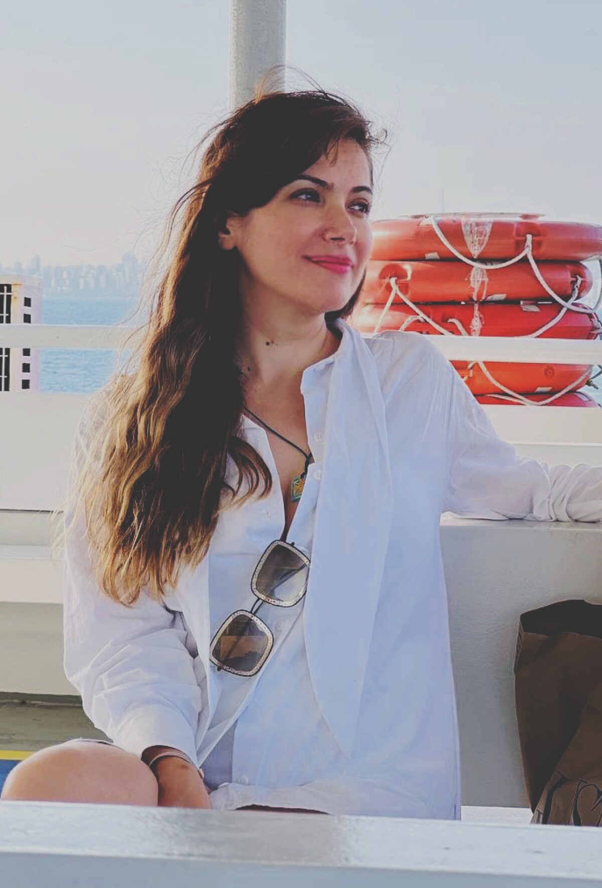 Mahdieh Allahviranloo is seen outside on a boat wearing a white shirt that has sunglasses clipped to it, she is sitting and looking to her left