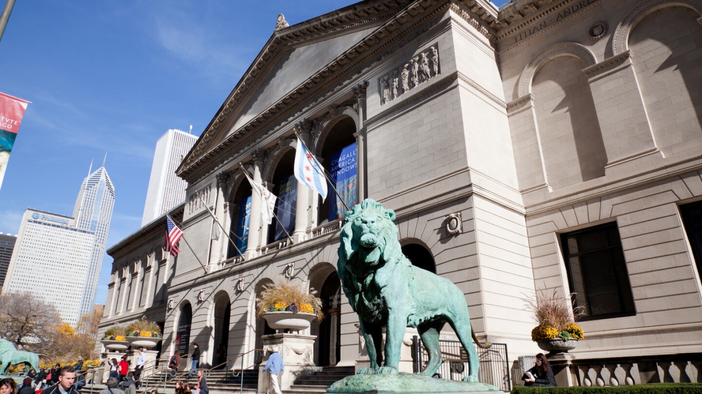 The exterior building of The Art Institute of Chicago at Michigan Avenue. There are people visible walking at the avenue.