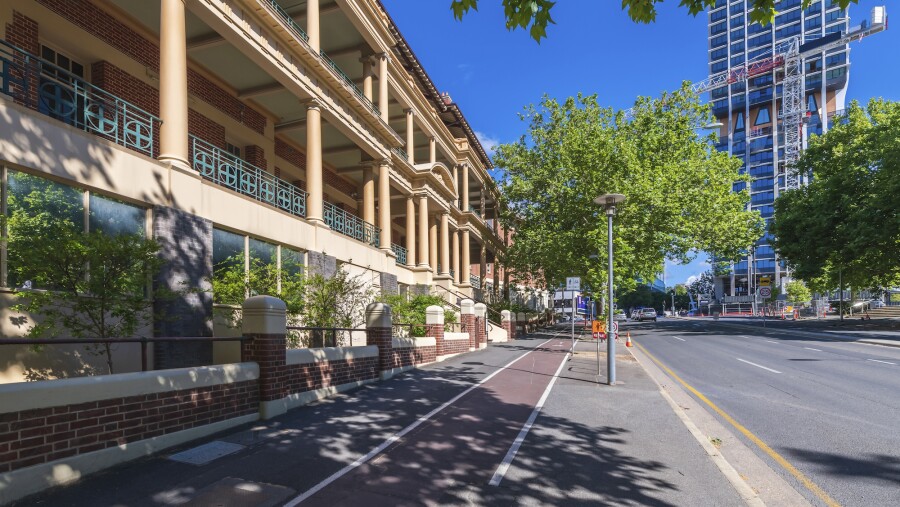 An angled street view of one side of the office building in Adelaide, Australia, including a brick wall, bike path, and trees