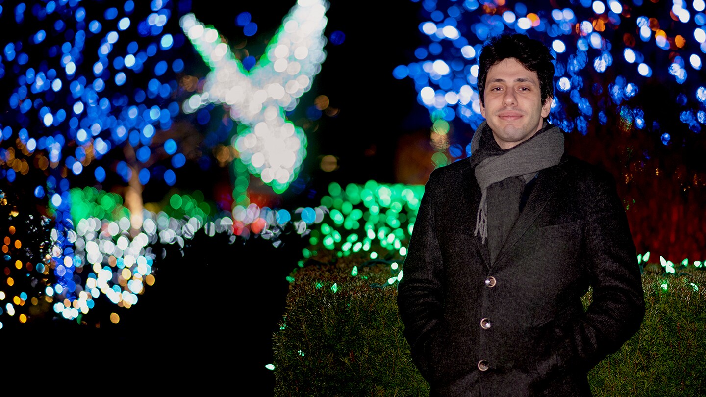 Alessandro Achille, a senior applied scientist at Amazon Web Services, is seen standing outside at night with a display of colored lights in the background