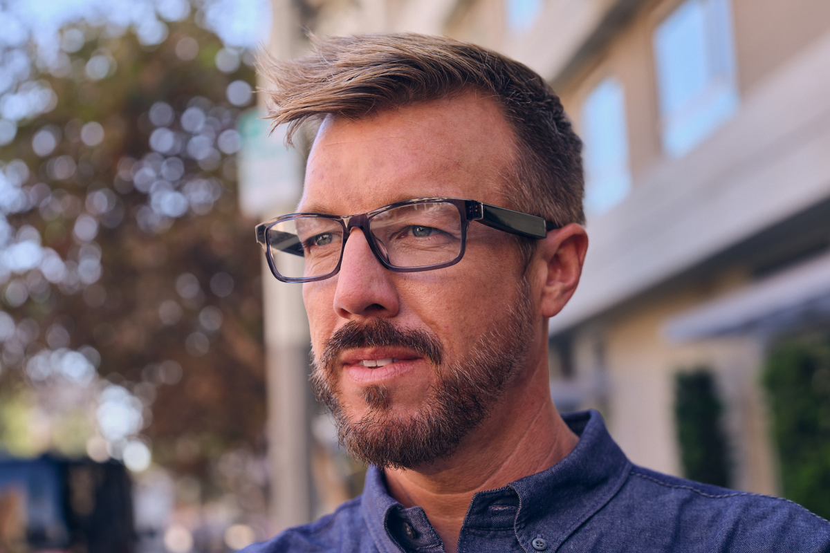 A man with a beard is seen wearing a pair of Echo Frames glasses. He is standing outside and is pictured in three-quarters view.