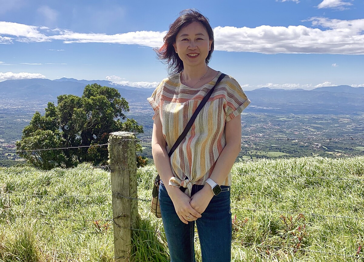 Belinda Zeng, the head of applied science and engineering at Amazon Search Science and AI, is seen standing outside in Costa Rica on a sunny day, a wire fence is just behind her in the foreground, and a valley and mountains are seen in the background