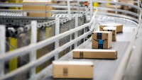 A line of Amazon packages are seen traveling down a conveyor belt