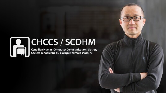 Richard Zhang, right, is seen with his arms crossed, facing the camera -- to the left is the logo for the CHCCS or Canadian Human-Computer Communications Society